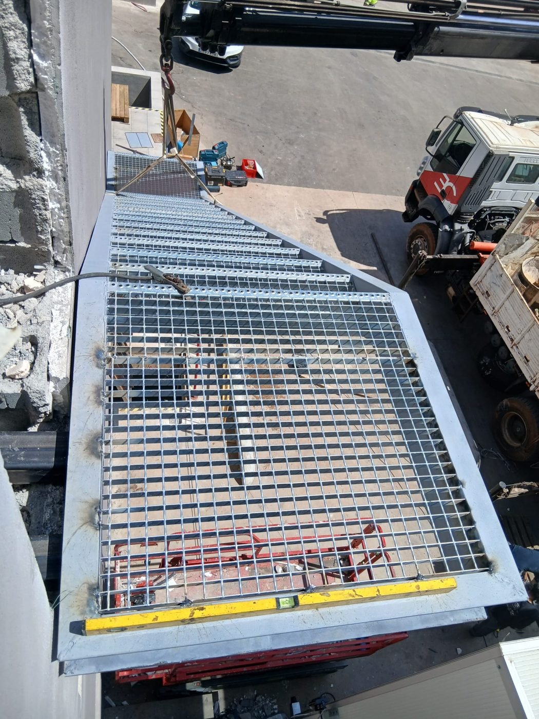 Rejilla metálica elevada con grúa durante el montaje en obra