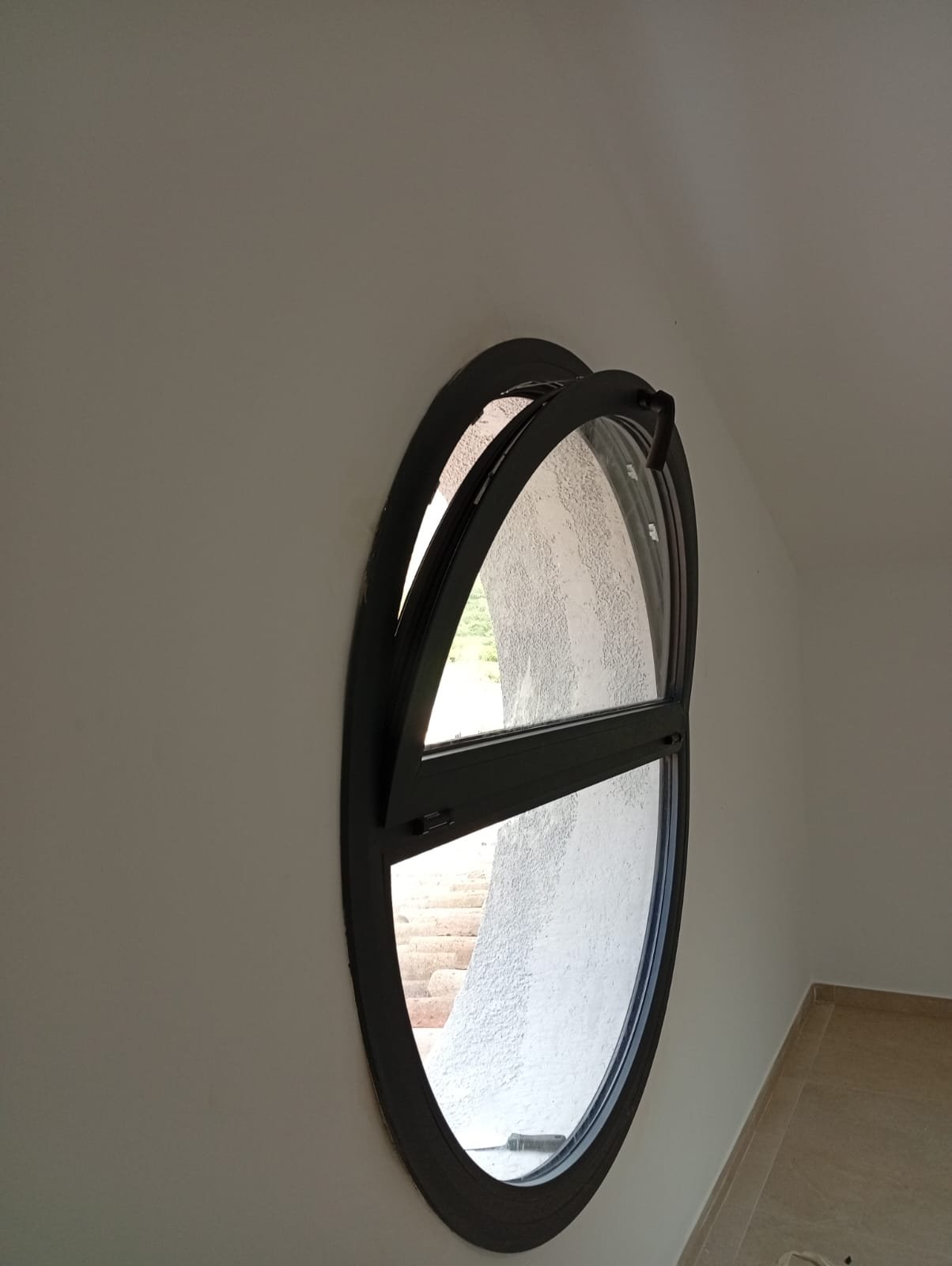 Ventana ovalada de aluminio negro abatible instalada en vivienda